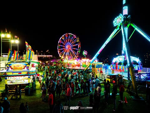 Lit Ferris wheel and swinging pendulum ride over the crowded midway at night, Pied Piper's Haunted Carnival 2023